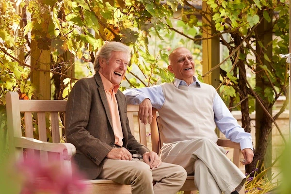 Two older men laughing together on a garden bench