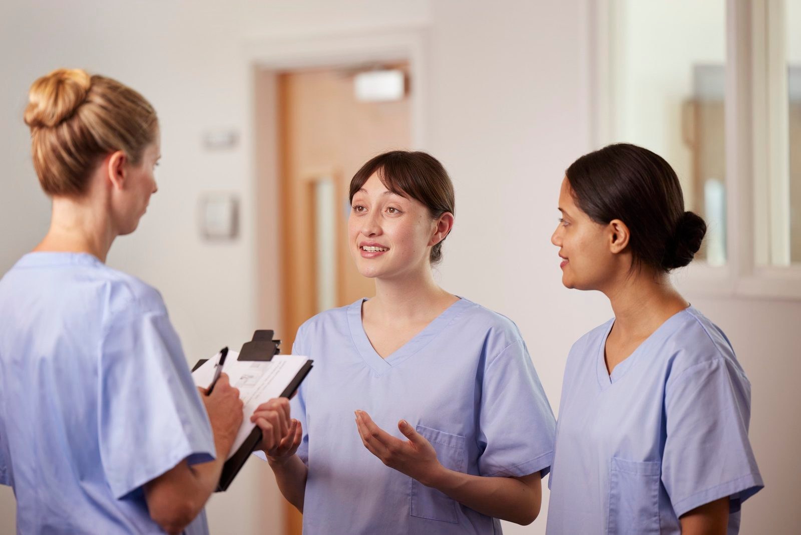 Florence: three nurses talking in a hospital corridor, one with a clipboard