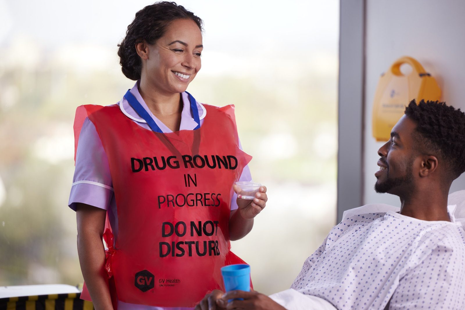 A nurse in a GV Health drug round tabard handing a patient his medicine, both smiling