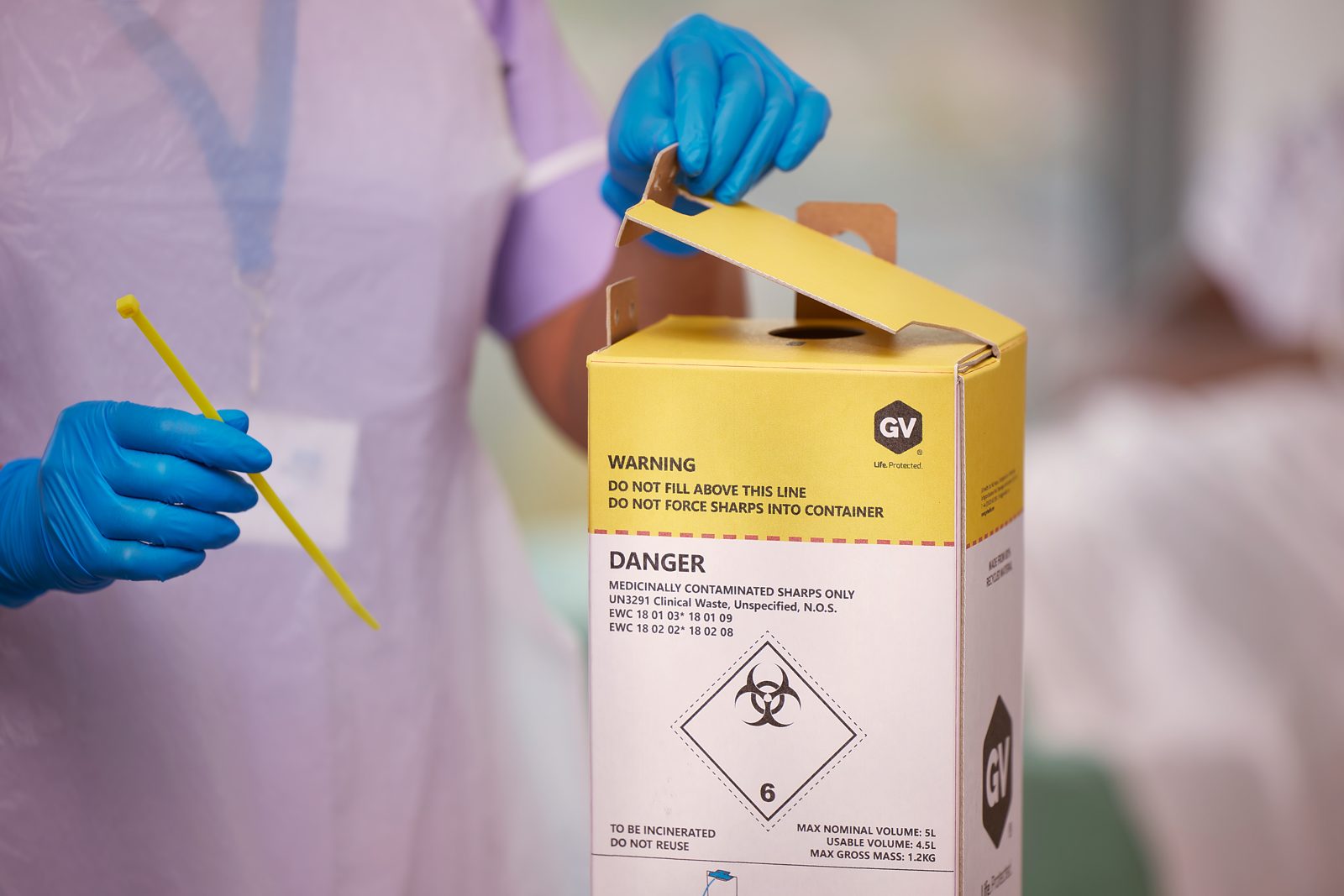 A gloved hand using a GV sharps box