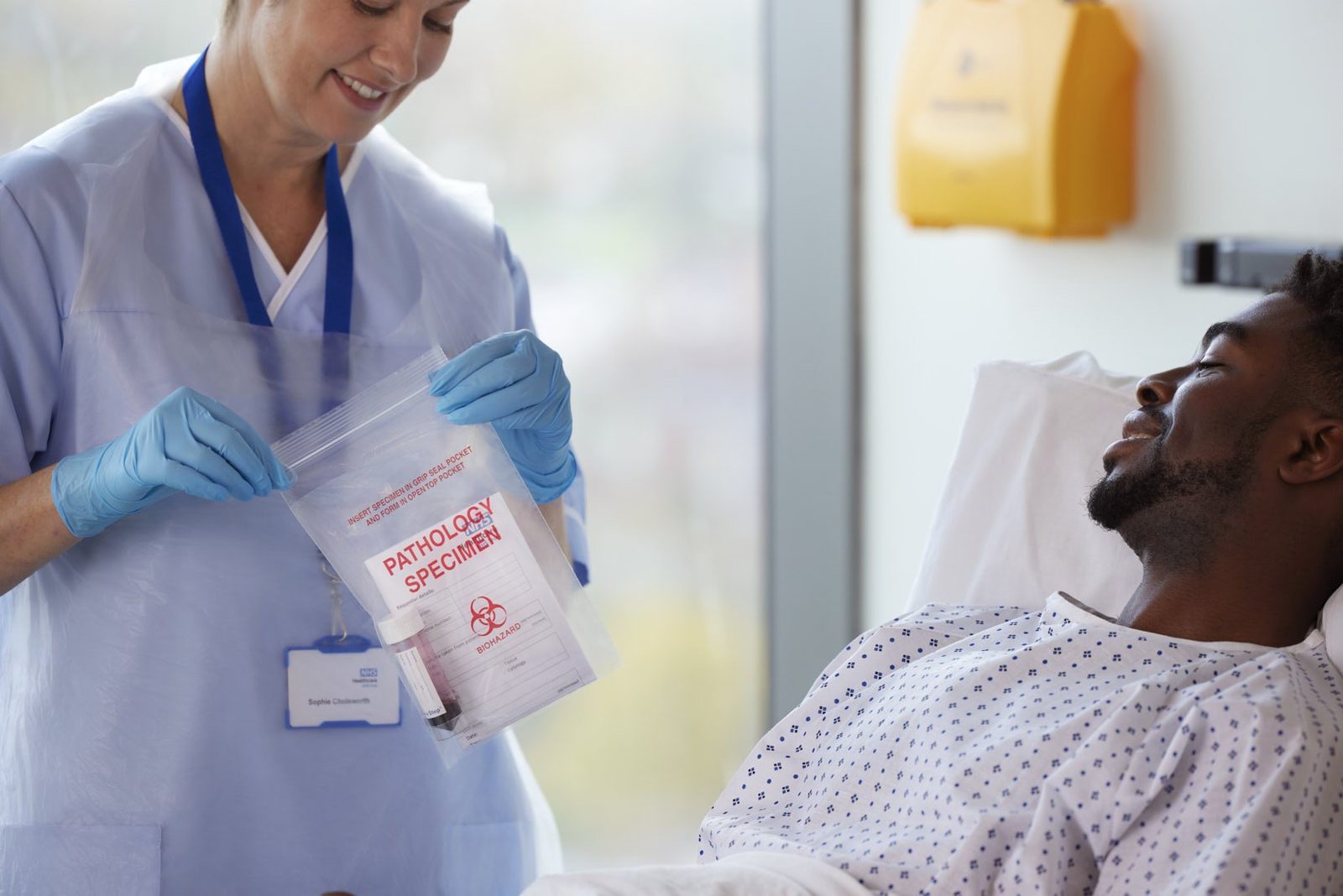 A nurse sealing a pathology specimen bag beside a smiling patient