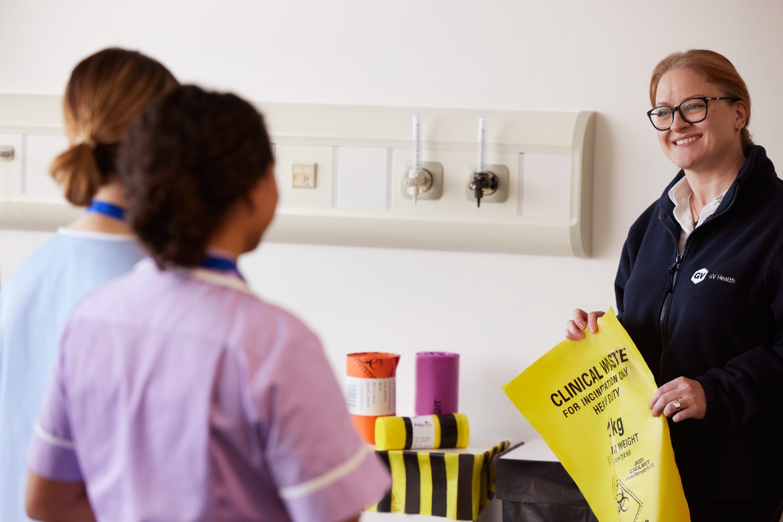 Two nurses and a waste collector exchanging a yellow clinical waste bag