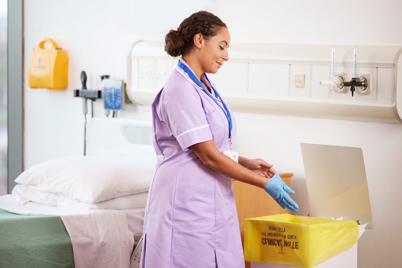 GV Health: a nurse putting a glove into a yellow clinical waste bin on a ward