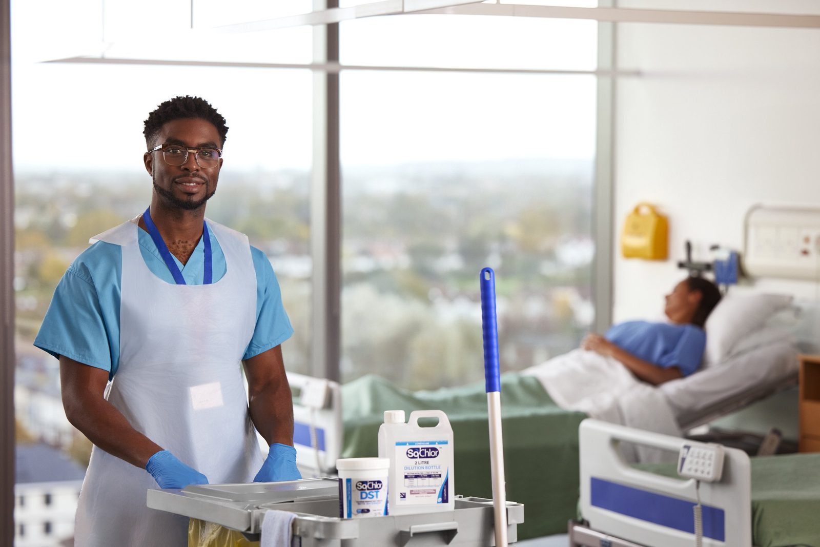 A cleaner beside a hospital bed with a trolley of SoChlor disinfectant